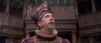 Movie still from “Shakespeare in Love” (1998), directed by John Madden – A man wearing a purple and gold hat and a beard; Close Up shot, Low angle