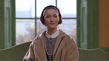 Movie still from “Shallow Grave” (1994), directed by Danny Boyle – A woman in a brown coat and a pearl necklace sitting in a chair; Close Up shot, Low angle
