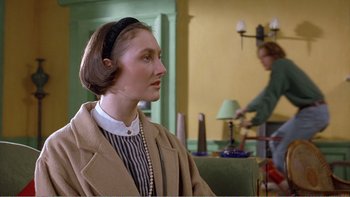 Movie still from “Shallow Grave” (1994), directed by Danny Boyle – A woman in a brown coat is sitting in front of a table; Medium shot, Over the shoulder angle