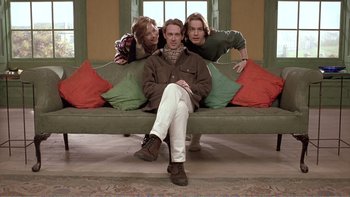 Movie still from “Shallow Grave” (1994), directed by Danny Boyle – A man sitting on top of a couch next to two other men; Medium shot, Low angle