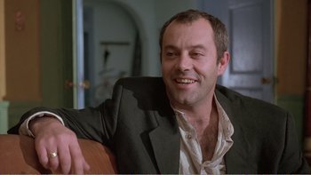 Movie still from “Shallow Grave” (1994), directed by Danny Boyle – A person wearing a suit and smiling; Close Up shot, Low angle