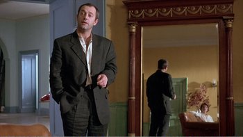 Movie still from “Shallow Grave” (1994), directed by Danny Boyle – A man standing in front of a mirror in front of a door; Medium shot, Low angle