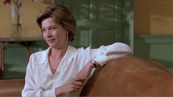 Movie still from “Shallow Grave” (1994), directed by Danny Boyle – A woman sitting on top of a couch wearing a white shirt; Medium shot, Low angle