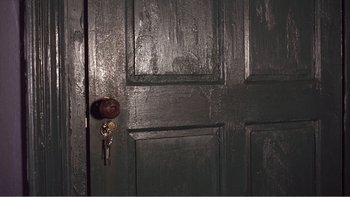 Movie still from “Shallow Grave” (1994), directed by Danny Boyle – A black door with a brown handle and a key in it; Extreme Close Up shot, Overhead angle