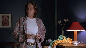 Movie still from “Shallow Grave” (1994), directed by Danny Boyle – A man standing in a room holding a cell phone; Medium shot, Low angle