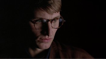 Movie still from “Shallow Grave” (1994), directed by Danny Boyle – A man wearing glasses and a brown jacket; Close Up shot, Low angle