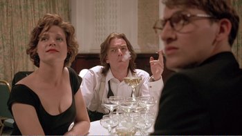 Movie still from “Shallow Grave” (1994), directed by Danny Boyle – Three people sitting at a dinner table smoking and drinking champagne; Medium shot, Low angle