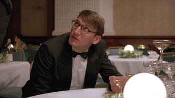 Movie still from “Shallow Grave” (1994), directed by Danny Boyle – A man sitting at a table with a glass of wine in front of him; Close Up shot, Low angle