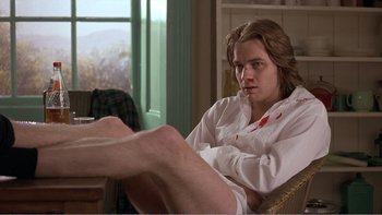 Movie still from “Shallow Grave” (1994), directed by Danny Boyle – A young man sitting on a chair with his legs crossed; Medium shot, High angle
