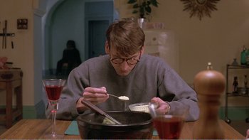 Movie still from “Shallow Grave” (1994), directed by Danny Boyle – A man sitting at a table with a bowl of food; Medium shot, High angle