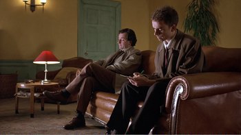 Movie still from “Shallow Grave” (1994), directed by Danny Boyle – A couple of men sitting next to each other on a couch; Medium shot, Low angle