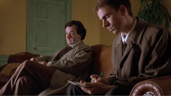 Movie still from “Shallow Grave” (1994), directed by Danny Boyle – Two men in suits sitting on a couch; Medium shot, Low angle