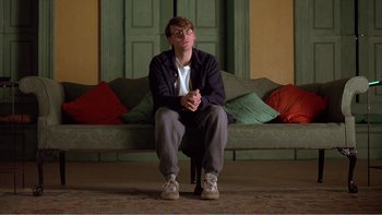 Movie still from “Shallow Grave” (1994), directed by Danny Boyle – A man sitting on the ground in front of a green door; Medium shot, Low angle