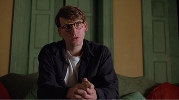 Movie still from “Shallow Grave” (1994), directed by Danny Boyle – A man sitting on a couch with his hands clasped together; Close Up shot, Low angle