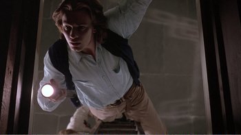 Movie still from “Shallow Grave” (1994), directed by Danny Boyle – A man standing on top of a ladder holding a flashlight; Medium shot, Low angle