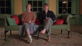 Movie still from “Shallow Grave” (1994), directed by Danny Boyle – A man and a woman sitting on a couch in front of a window; Wide shot, Low angle