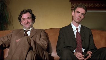 Movie still from “Shallow Grave” (1994), directed by Danny Boyle – A couple of men sitting on top of a brown couch; Medium shot, Low angle