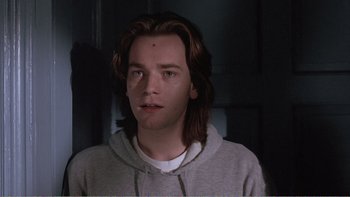 Movie still from “Shallow Grave” (1994), directed by Danny Boyle – A man with long brown hair wearing a gray hoodie; Close Up shot, Low angle