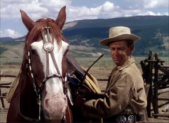 Movie still from “Shane” (1953), directed by George Stevens – A man standing next to a horse in a field; Medium shot, Low angle
