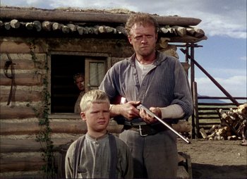 Movie still from “Shane” (1953), directed by George Stevens – A man and a young boy in front of a log cabin; Medium shot, Low angle