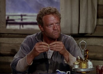 Movie still from “Shane” (1953), directed by George Stevens – A man sitting at a table with a cigarette in his mouth; Close Up shot, Low angle