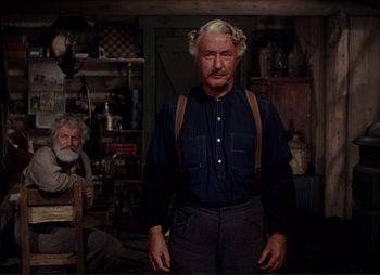 Movie still from “Shane” (1953), directed by George Stevens – An older man in a blue shirt is standing next to an older man; Medium shot, Over the shoulder angle
