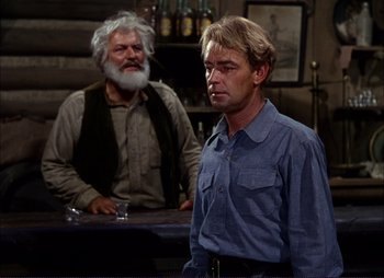 Movie still from “Shane” (1953), directed by George Stevens – A man standing next to another man at a bar; Medium shot, Over the shoulder angle