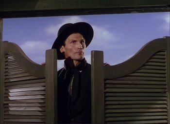 Movie still from “Shane” (1953), directed by George Stevens – A man wearing a black hat standing next to a wooden fence; Medium shot, Low angle
