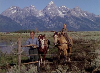 Movie still from “Shane” (1953), directed by George Stevens – A man and a woman on horses in a field with mountains in the background; Wide shot, Low angle