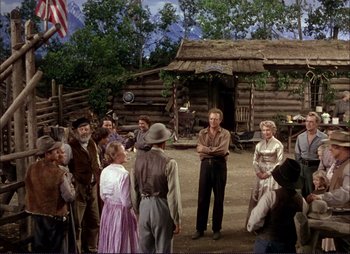Movie still from “Shane” (1953), directed by George Stevens – A group of people standing in front of a log cabin; Wide shot, Over the shoulder angle