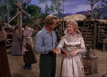 Movie still from “Shane” (1953), directed by George Stevens – A man and a woman holding hands in front of a group of people; Medium shot, Low angle