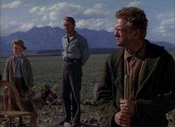Movie still from “Shane” (1953), directed by George Stevens – Two men and a dog stand in a field with mountains in the background; Wide shot, Low angle