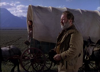 Movie still from “Shane” (1953), directed by George Stevens – A man standing in front of a covered wagon; Wide shot, Low angle