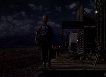 Movie still from “Shane” (1953), directed by George Stevens – A man standing in front of a wooden structure; Wide shot, Low angle