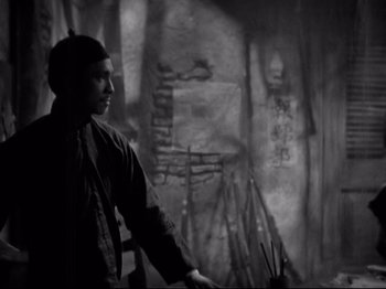 Movie still from “Shanghai Express” (1932), directed by Josef von Sternberg – A man standing next to a wall in a room; Medium shot, High angle