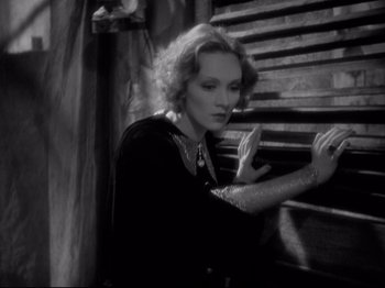 Movie still from “Shanghai Express” (1932), directed by Josef von Sternberg – An old photo of a woman leaning against a wooden stair railing; Medium shot, Low angle