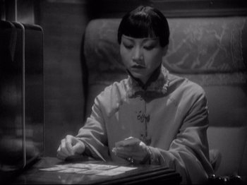 Movie still from “Shanghai Express” (1932), directed by Josef von Sternberg – A woman sitting at a table looking down at a piece of paper; Medium shot, Over the shoulder angle