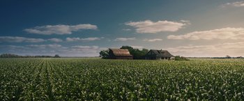 A field with a house and barn in the background