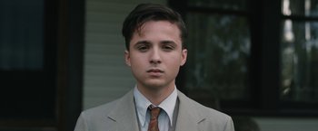 Movie still from “1922” (2017), directed by Zak Hilditch – A man in a suit and tie standing outside of a building; Close Up shot, Low angle