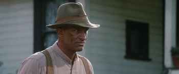 Movie still from “1922” (2017), directed by Zak Hilditch – A man wearing a hat standing in front of a building; Close Up shot, Low angle