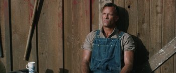 Movie still from “1922” (2017), directed by Zak Hilditch – A man wearing overalls standing next to a wooden wall; Close Up shot, Low angle