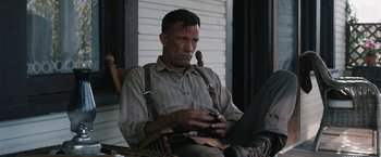 Movie still from “1922” (2017), directed by Zak Hilditch – A man sitting on a porch looking at his cell phone; Medium shot, Low angle