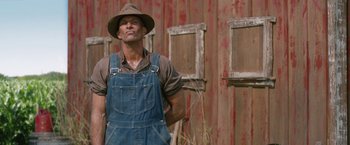 Movie still from “1922” (2017), directed by Zak Hilditch – A man in a hat and overalls standing in front of a barn; Medium shot, Low angle