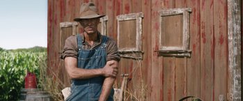 Movie still from “1922” (2017), directed by Zak Hilditch – A man wearing a hat standing in front of an old barn; Medium shot, Low angle