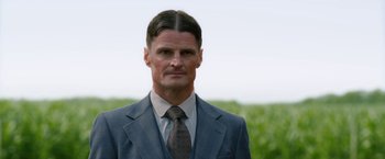 A man in a suit and tie standing in front of a field