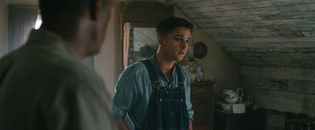 Movie still from “1922” (2017), directed by Zak Hilditch – A young man wearing overalls standing next to a mirror; Medium shot, Over the shoulder angle