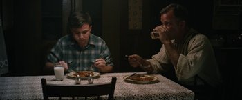 Movie still from “1922” (2017), directed by Zak Hilditch – Two people sitting at a table eating food; Medium shot, High angle