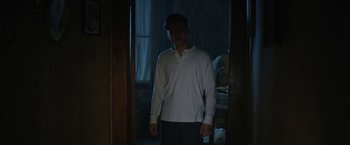 Movie still from “1922” (2017), directed by Zak Hilditch – A man standing in a dark room in front of a window; Medium shot, Low angle