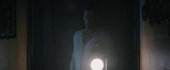 Movie still from “1922” (2017), directed by Zak Hilditch – A man standing in a dark room holding a light; Medium shot, Low angle