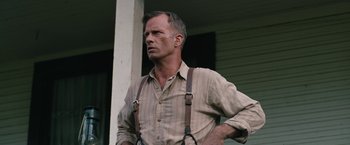 Movie still from “1922” (2017), directed by Zak Hilditch – A person wearing suspenders near a building; Close Up shot, Low angle
